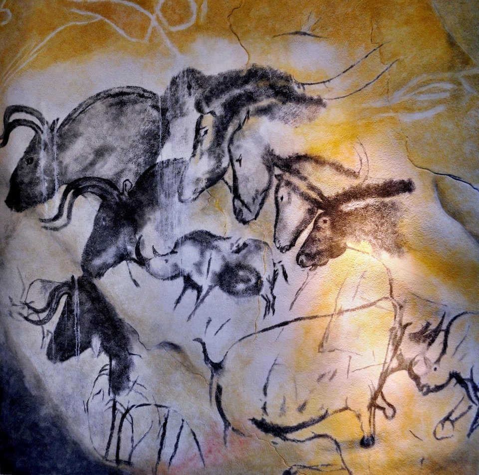 Black charcoal drawings of overlapping horse heads on the ochre wall of the Chauvet Cave.